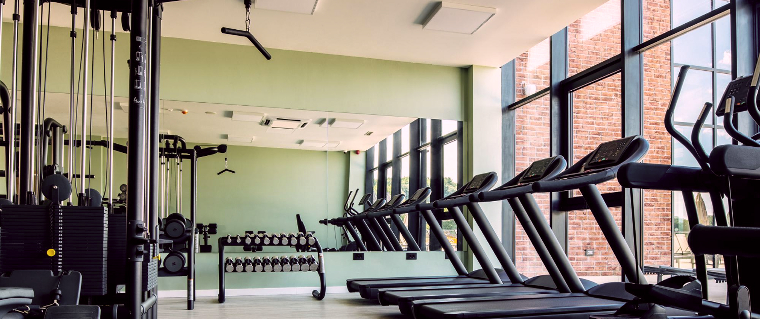 фото тренажерного зала с большими панорамными окнами, у окон беговые дорожки, с другой стороны тренажёры со свободными весами